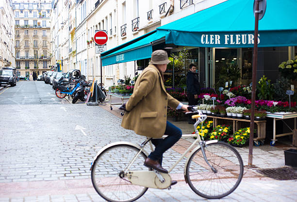 Paris, France - March 23, 2025: A senior cyclist in a bowler hat on Rue Cler in the 7th arrondissement. The street is only for cyclists and pedestrians, and is known for its gourmet food and cafes.