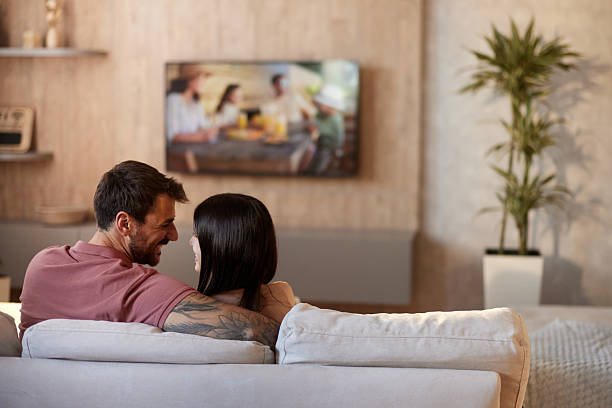 istock Back view of embraced couple talking while watching TV at home. 2224999572