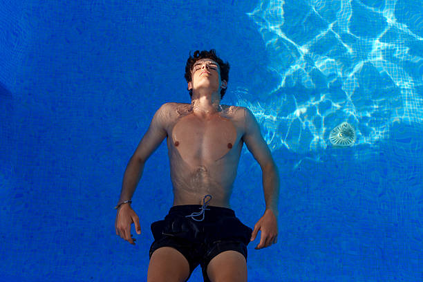 Young man floating in a vibrant blue swimming pool, savoring the joys of summer holidays and embracing a carefree, relaxing lifestyle
