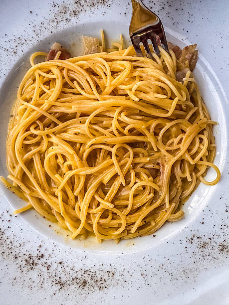 A delicious plate of creamy spaghetti carbonara served on a white dish, accompanied by vibrant side dishes and refreshing drinks in the background, set on an elegant dining table