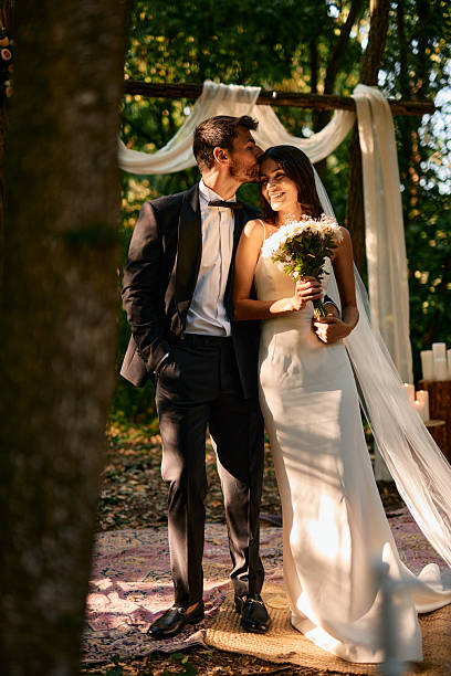 istock Groom kissing bride on forehead during forest wedding ceremony 2225009549