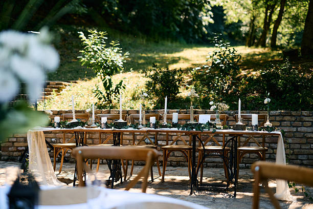 Elegant wedding reception table setting with candles, greenery, and rustic wooden chairs in a beautiful garden setting, creating a romantic ambiance