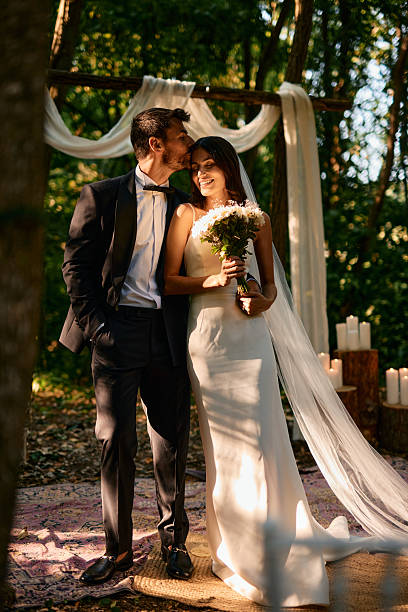 istock Groom kissing bride on forehead during wedding ceremony in the forest 2225010365