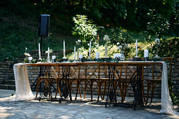 Rustic wedding table setting featuring vintage sewing machine bases as table legs, adorned with candles, flowers, and greenery, creating a charming ambiance for an outdoor celebration