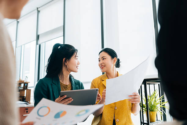 istock Two confident young Asian businesswomen using digital and checking documents during the meeting. Discussing strategy, the company mission and vision for the future. 2225011389