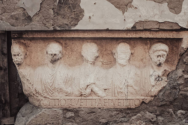 Capua, Italy – An ancient Roman bas-relief, depicting five male figures in togas, emerges embedded in the base of an abandoned building. Visibly worn by time, the work is an example of historical stratification, where the archaeological past coexists with contemporary urban decay.