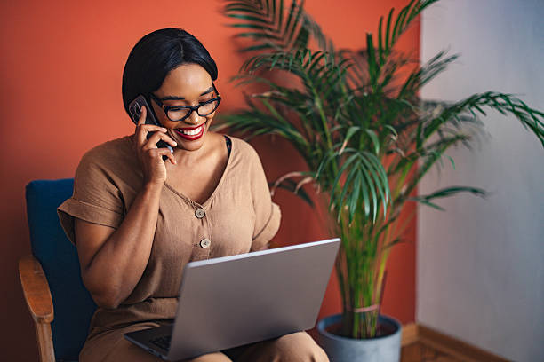 istock Smiling Woman Working on Laptop While Talking on the Phone at Home 2225013891