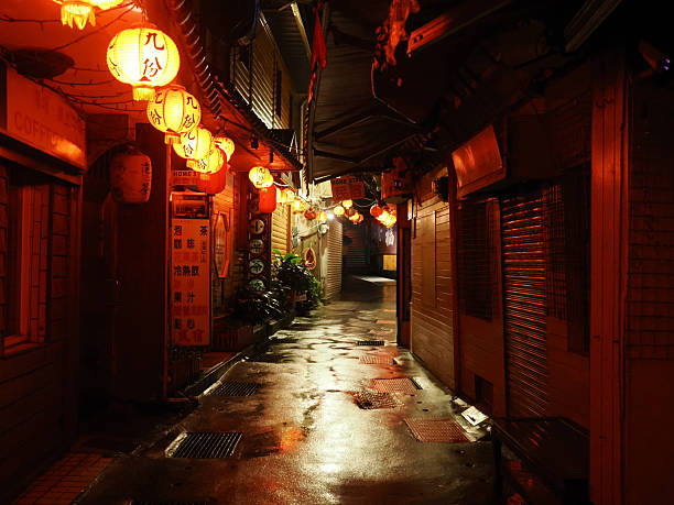 Jiufen, Taiwan - November 8, 2024 - A dark, wet, and reflective alleyway in Jiufen Old Street, illuminated by warm glowing traditional lanterns and creating a serene, moody atmosphere at night.