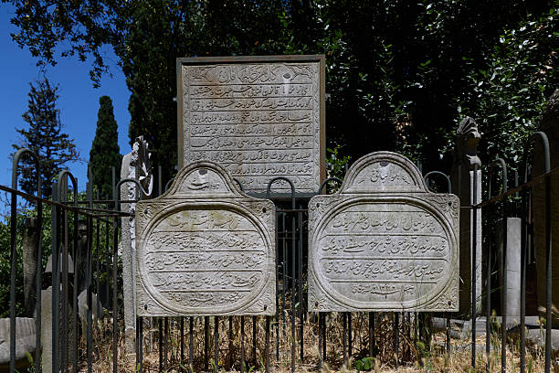 Istanbul, Turkey - July 15, 2025: View of Ottoman-era gravestones featuring detailed Arabic script inscriptions, located within an iron fence at Yahya Efendi Cemetery in Besiktas. These historical tombstones date back to the late Ottoman period and reflect the classical Islamic style of funerary desig