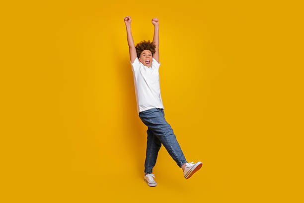 istock Happy young boy in casual attire expressing excitement while jumping against a bright yellow background with cheerful energy 2225017568