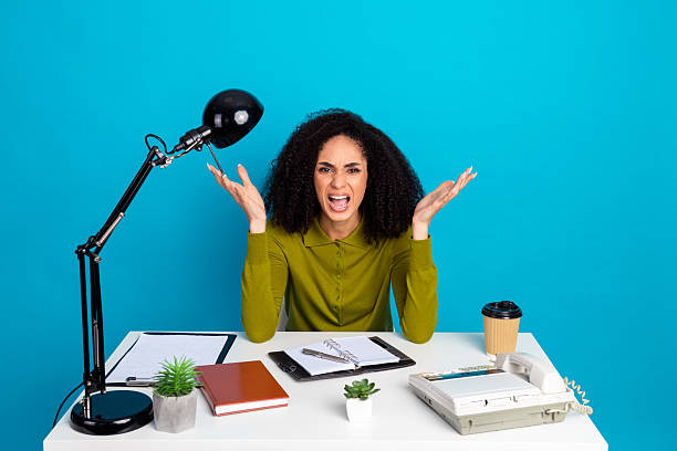 istock Frustrated young woman working at office desk with props on blue background expressing emotions 2225018947