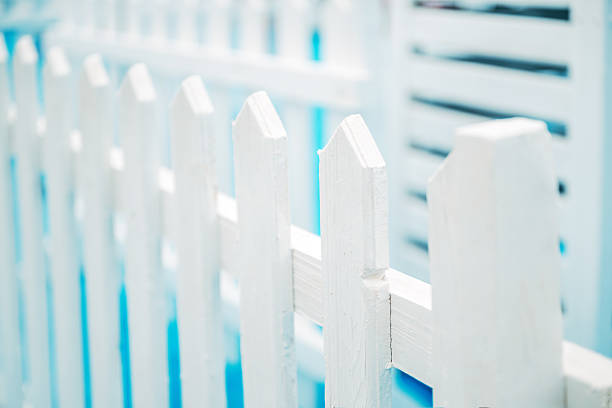 White fence with decorative lamps. Close-up view of a white picket fence with spherical decorative lamps on a blurred green background, creating a feeling of peace, suburbia