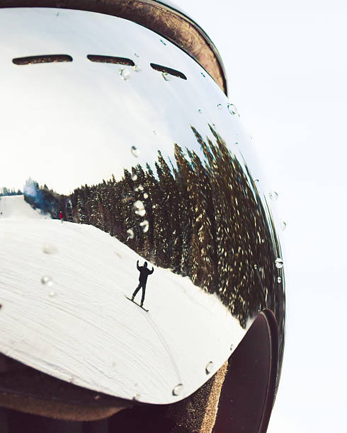 Snowboarder carving snowy slope reflected in ski goggles with water drops, pine forest under clear winter sky, concept extreme sport, safety, perspective.