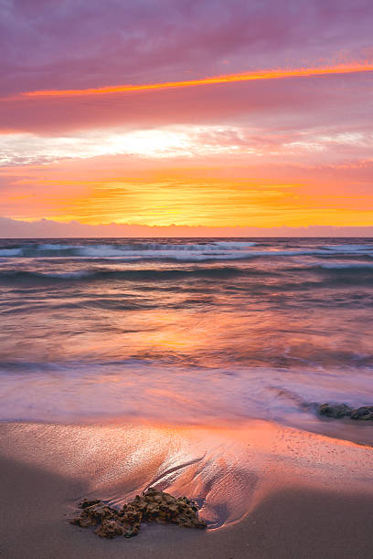 istock Colorful ocean waves at sunset with rocks on the sandy shore 2225030235