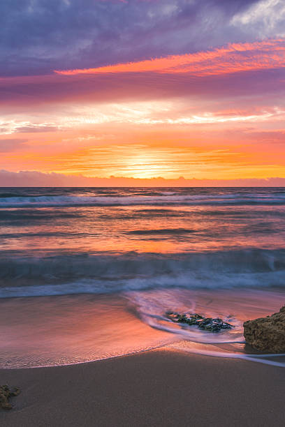 istock Colorful ocean waves at sunset with rocks on the sandy shore 2225030397