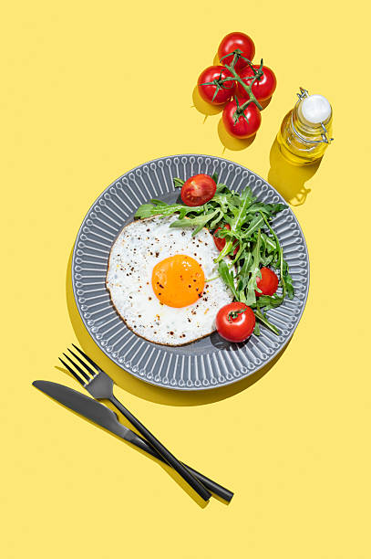 istock Fried eggs with arugula and cherry tomatoes on a dark plate on a yellow background with cultery 2225031749