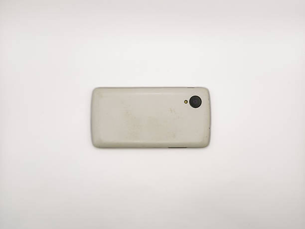 A white cell phone is laying on a white surface. copy space, flay lay, top view. The back of the phone is missing. The phone is not in use