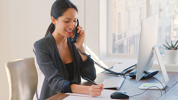 istock Young Businesswoman Working At Desk On Computer Talking On Phone 2225036964