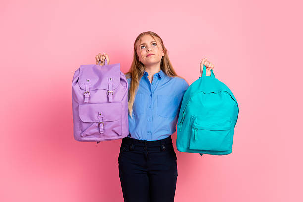 istock Smiling girl holding two backpacks making choices on a pink background 2225038455