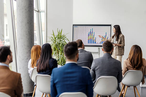 istock Young female analyst is standing near interactive board and showing charts and statistics to audience. 2225041040