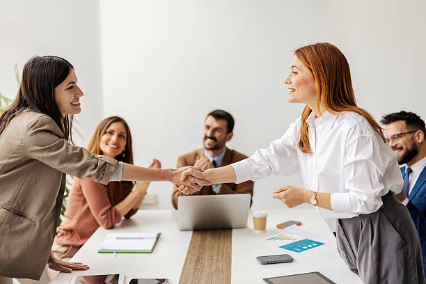 istock Two female executives shaking hands and congratulating on a success in front of businesspeople who are applauding in a boardroom. 2225041846