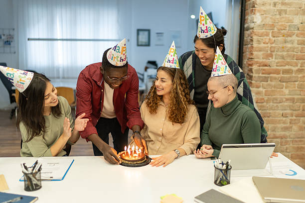 istock Colleagues lighting candles on birthday cake in office 2225043407
