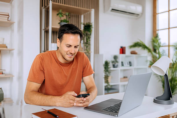 istock Young smiling casually clothed man text messaging on smart phone while working at home office 2225047086