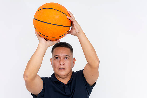 A skilled middle aged man looking laser focused while poised to shoot a 3 pointer with a basketball. Dressed in a casual polo shirt.