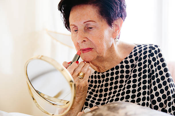 istock Elderly woman applying lipstick while looking in a mirror 2225055761