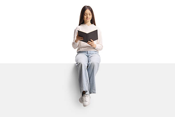 istock Teenage girl sitting on a blank panel and reading a book 2225056260