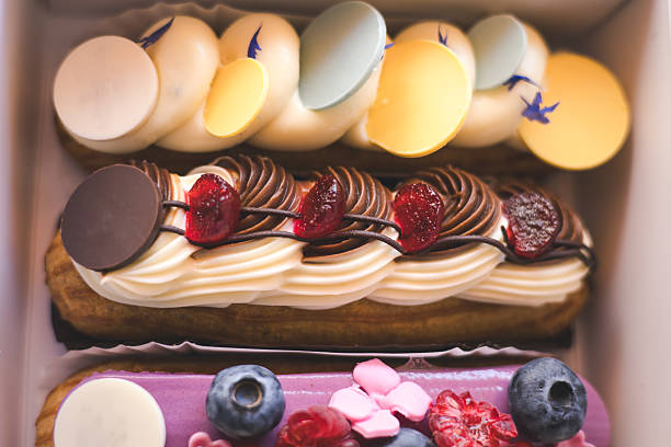 Delicious eclairs with fresh berries and macarons beautifully displayed in a bakery box. A close-up of colorful eclairs, adorned with fresh berries, and decorative frosting. Creamy sweets and treats.