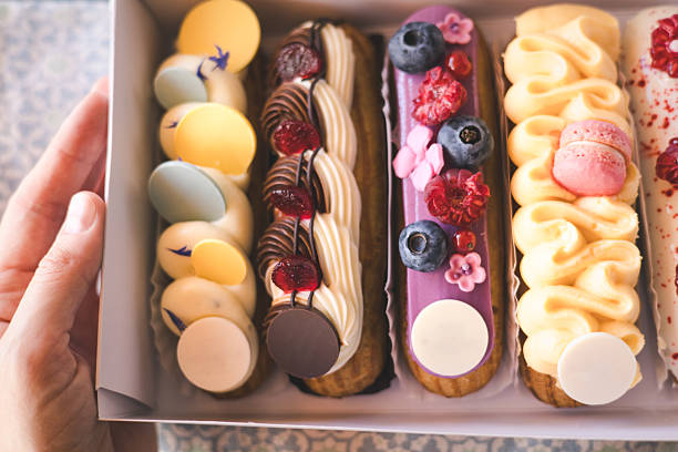 istock Delicious eclairs with fresh berries and macarons beautifully displayed in a bakery box. A close-up of colorful eclairs, adorned with fresh berries, and decorative frosting. Creamy sweets and treats. 2225057271