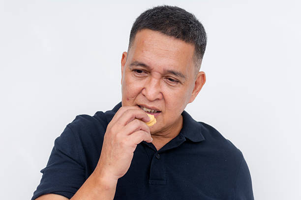istock A middle aged asian man munches on a biscuit. Having a quick snack, posing on a white background. 2225058878