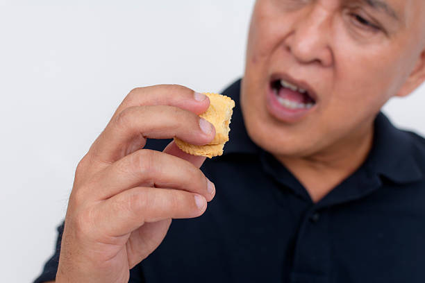 A middle aged asian man munches on a biscuit. Having a quick snack, posing on a white background.