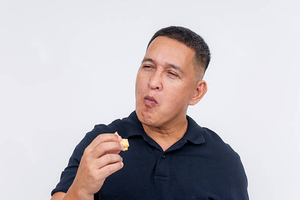 istock A middle aged asian man munches on a biscuit. Having a quick snack, posing on a white background. 2225058885
