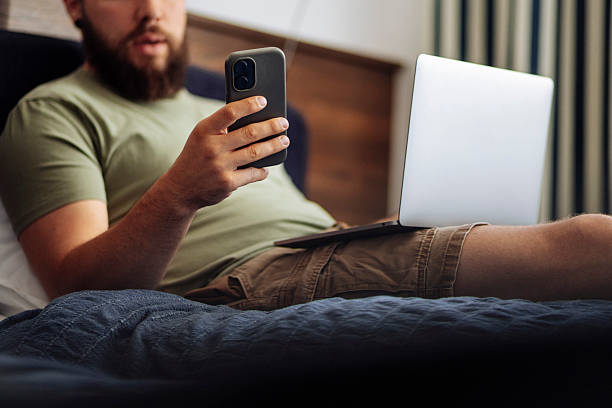 istock Man Using Smartphone and Laptop in Bedroom 2225063165