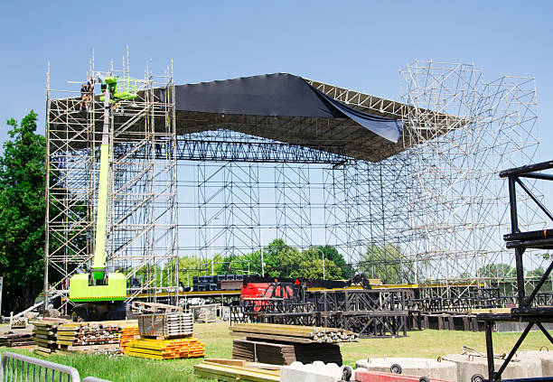 istock Stage construction for an outdoor concert. Workers on a lift and scaffolding are assembling the roof structure of a large stage.Music festival or major open-air event. 2225063726