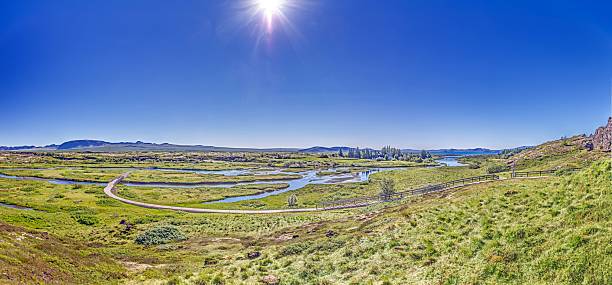 River landscape with walking path and green plains in Thingvellir National Park Iceland under bright sky