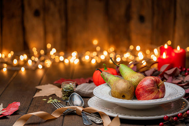 istock Cozy Autumnal vintage place setting on rustic table. Fruits, pumpkins and nuts with fallen leaves. Thanksgiving decoration on illuminated background 2225067394
