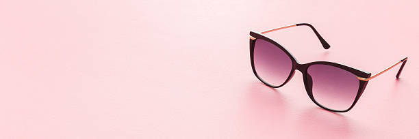 istock Female sunglasses with dark black plastic frame on light pink table background. Pastel color. Closeup. Wide banner. Empty place for text. 2225067785