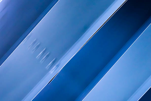 Metallic sheets pass through a coating process, reflecting hues of blue in an industrial setting.