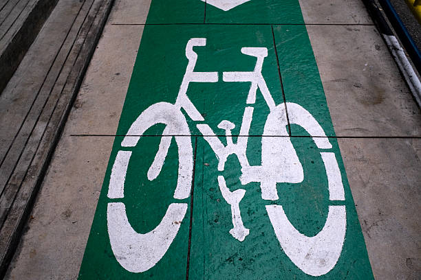 A clearly marked bicycle lane runs along a paved surface, defined by a vivid green stripe and a bold white bicycle symbol. The slightly worn texture of the concrete or asphalt suggests regular use, emphasizing the lane’s functional role in promoting safe, urban cycling.