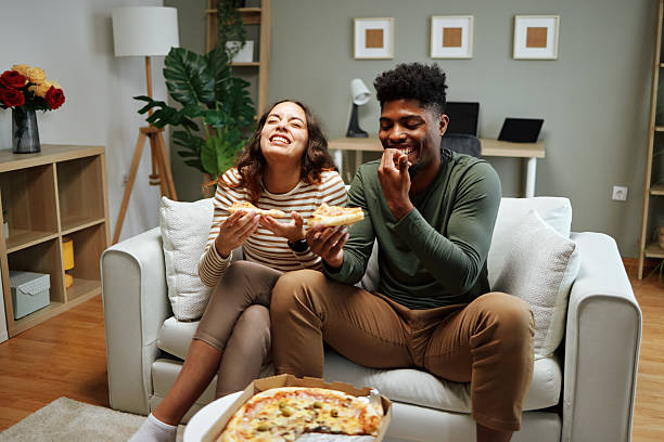 istock Happy couple laughing and eating pizza on sofa at home 2225075332