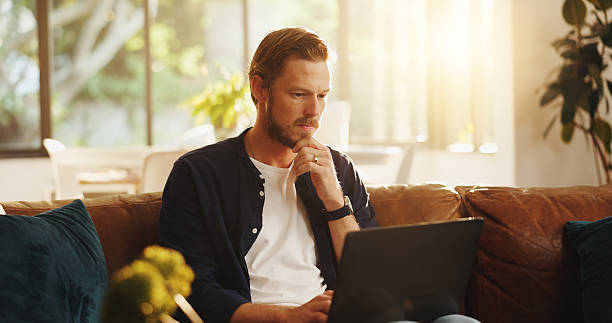 istock Man, website and reading on sofa with laptop, writer and thinking for script draft in home. Person, editor and technology in living room for research, networking and application with freelancer 2225080182