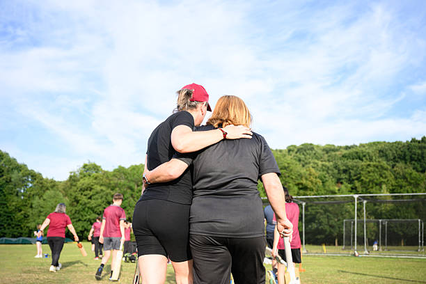 Mixed age range of women and girls practicing cricket on warm summer evening on a grass cricket pitch