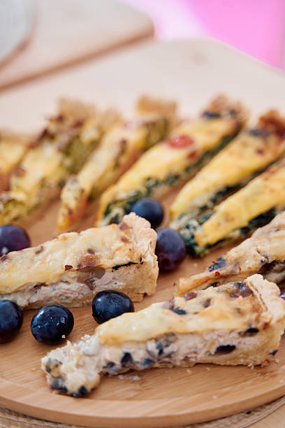 A wooden board displays an assortment of savory quiche slices accompanied by fresh blueberries, showcasing a colorful and delicious combination for brunch or a light meal.