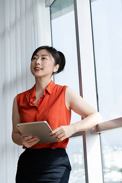 istock Smiling businesswoman using digital tablet in front of office window 2225082788