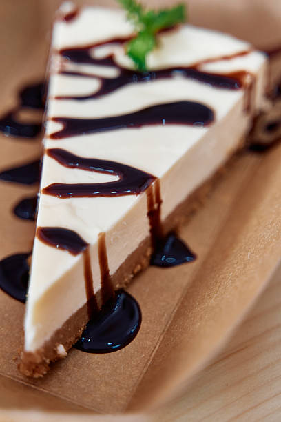 A luscious cheesecake slice drizzled with chocolate syrup rests on a brown plate, showcasing a smooth texture and crumbly crust, perfect for dessert lovers.