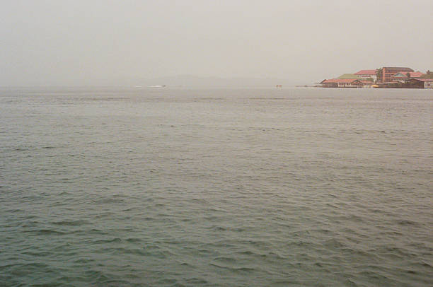 Tranquil ambiance of a clear sea extending to the horizon, with colorful buildings along the coast. Taken on 35mm film at Bocas del Toro, Panama during a foggy day.