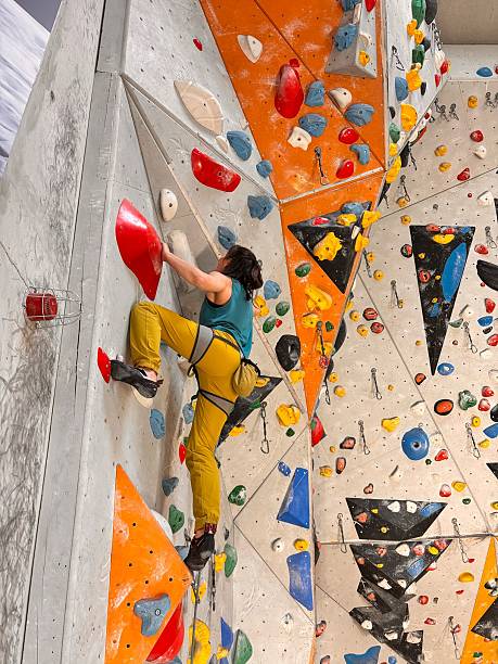 istock Female Climber On Indoor Climbing Wall With Colorful Holds And Harness: Dynamic Training Scene In Modern Bouldering Gym With Vertical Routes And Safety Equipment 2225088626